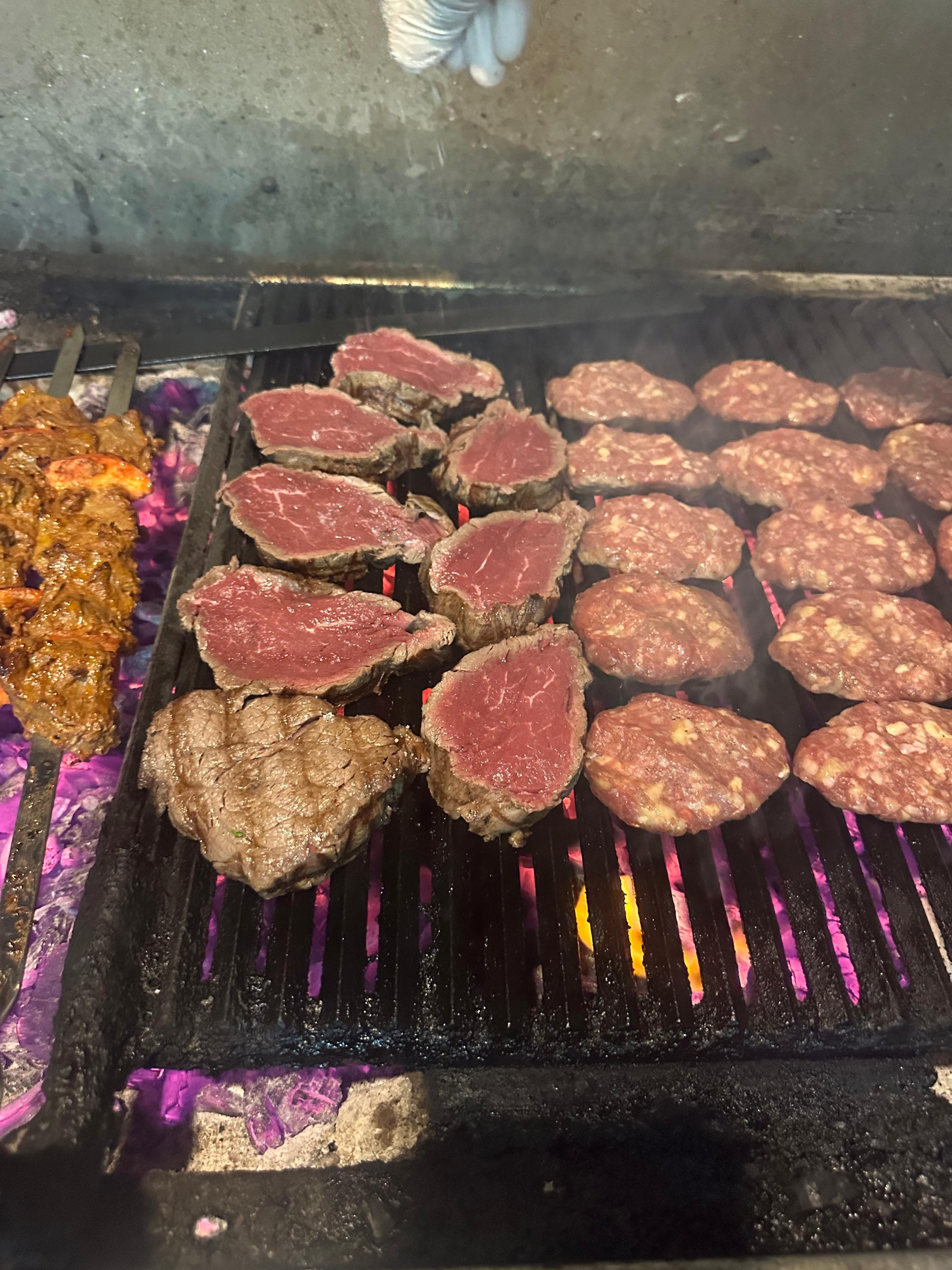 Steaks and burger patties searing side by side on the charcoal grill