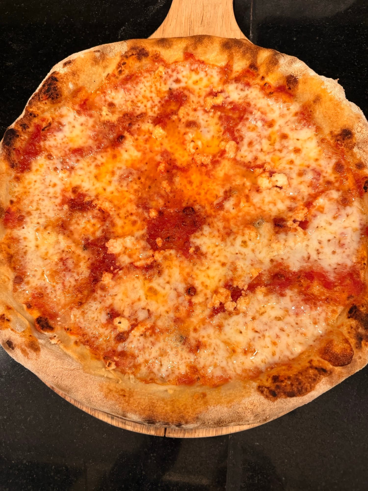 Wood-fired margherita pizza on a serving paddle